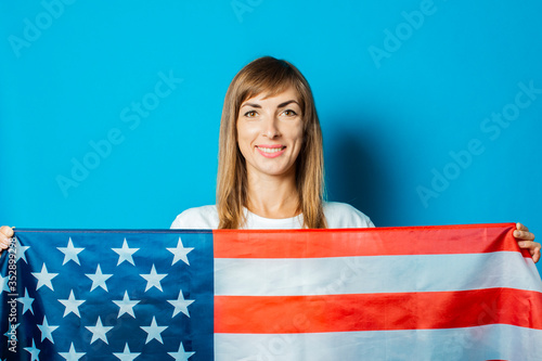 Young woman holds the USA flag in front of her on a blue background. USA Visa Concept, English, Independence Day, July 4th, Memorial Day. Travel to the USA