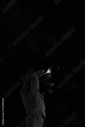 hand in black glove holding a black teaspoon on black background