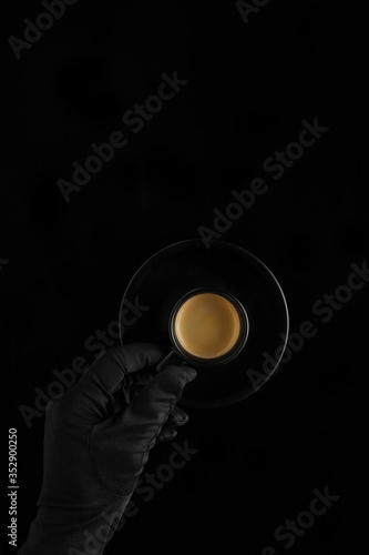 hand in black glove holding a black coffee cup with coffee on black background
