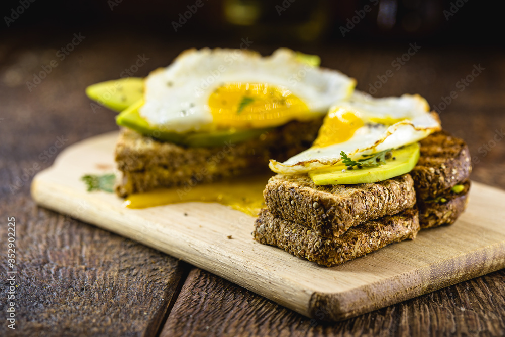 healthy breakfast, gluten-free bread, with slices of avocado cut on whole toast and fried egg. healthy breakfast, gluten-free bread, with slices of avocado cut on whole toast and fried egg.