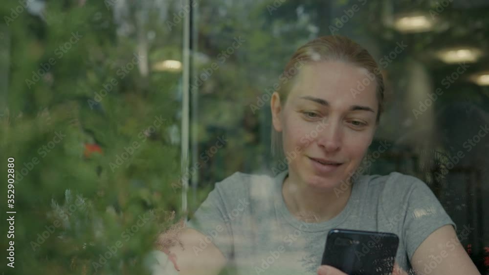 A woman drinks coffee in a cafe and uses a smartphone The view through the glass A woman drinks coffee in a cafe and uses a smartphone The view through the glass