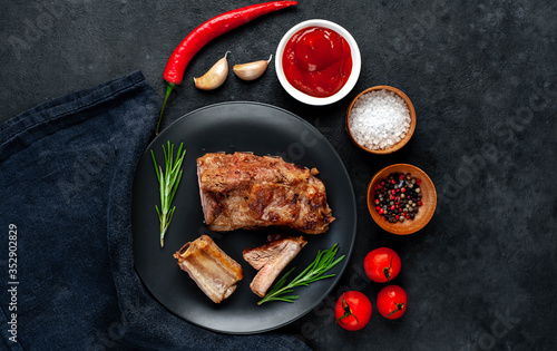 Grilled pork ribs on a black plate with spices on a stone background