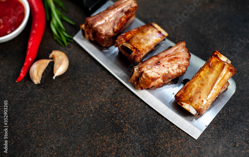 Grilled pork ribs over meat knife with spices on a stone background with copy space for your text