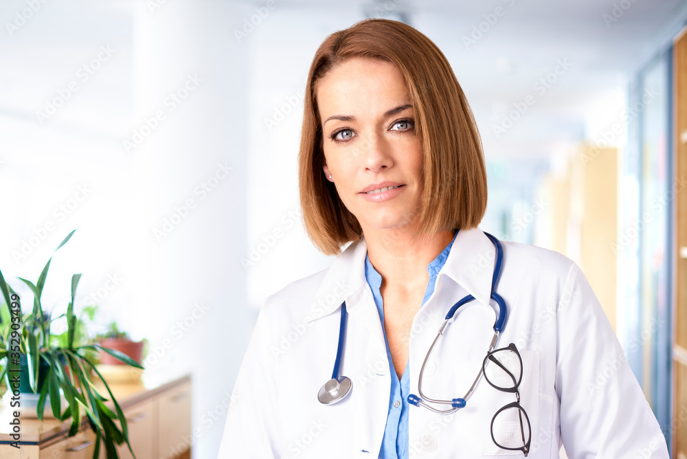 Female doctor looking at camera and smiling while standing in the hospital corridor Female doctor looking at camera and smiling while standing in the hospital corridor