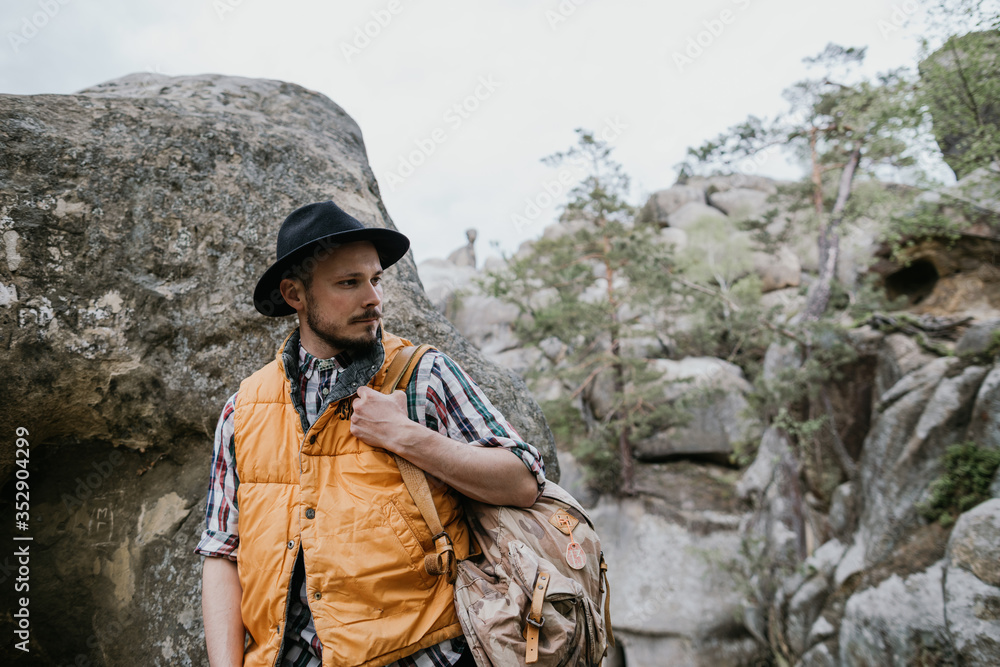 Portrait of a bearded hipster man in a hat with a backpack in the mountains.
