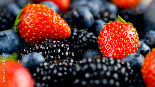 Macro photo of tasty sweet strawberry, blackberry and blueberry lying in heap on table. Assortment of berries