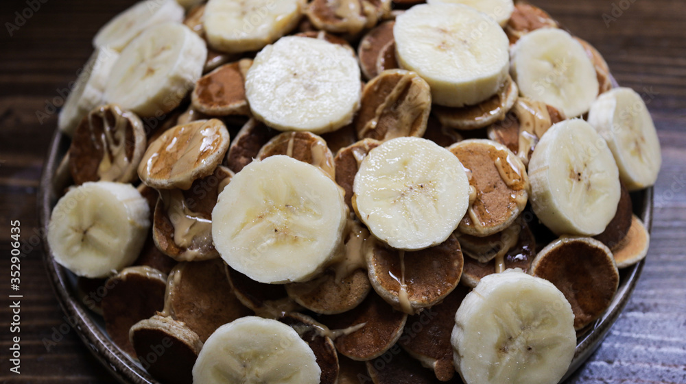 A plate of poffertjes, traditional Dutch Mini Pancakes served with honey, peanut butter and banana on the wooden background A plate of poffertjes, traditional Dutch Mini Pancakes served with honey, peanut butter and banana on the wooden background