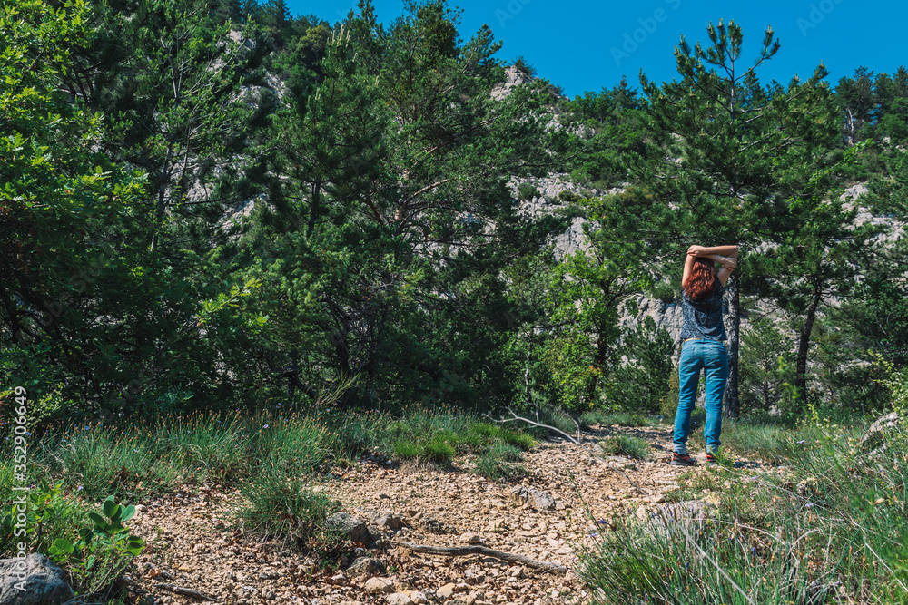 A full body shot of an unrecognizable young Caucasian female hiker standing with arms up on a path in the French Alps mountains on a sunny summer day A full body shot of an unrecognizable young Caucasian female hiker standing with arms up on a path in the French Alps mountains on a sunny summer day