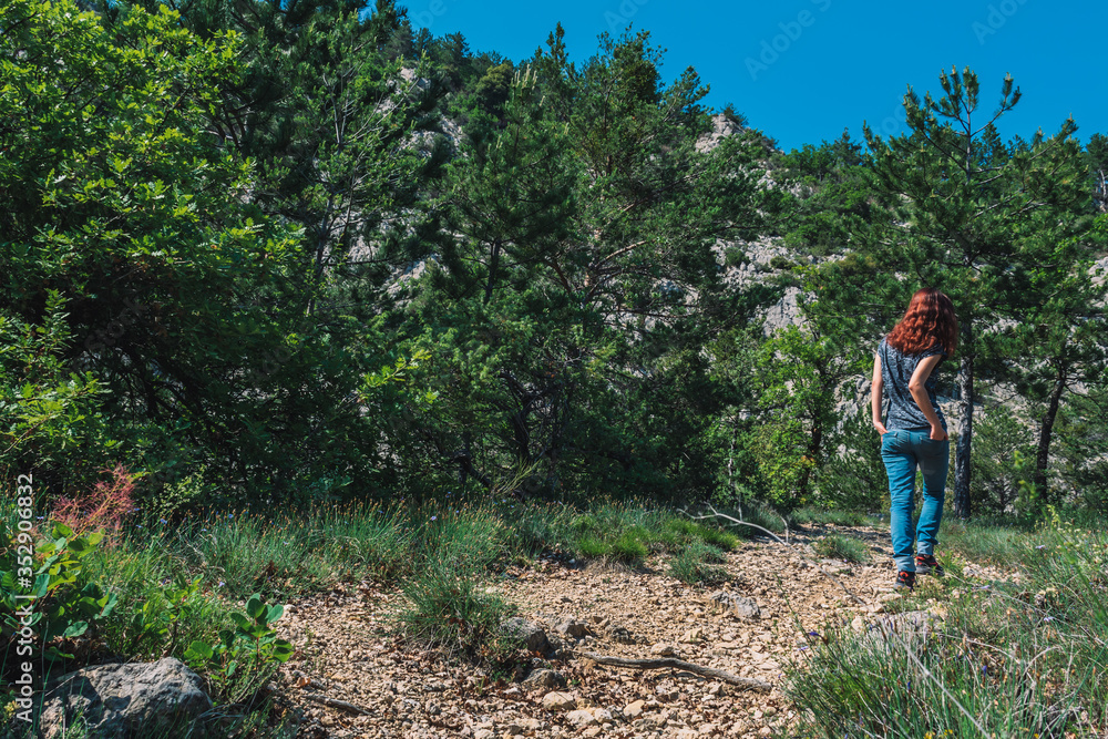 A full body shot of an unrecognizable young Caucasian female hiker walking up a path in the French Alps mountains on a sunny summer day A full body shot of an unrecognizable young Caucasian female hiker walking up a path in the French Alps mountains on a sunny summer day