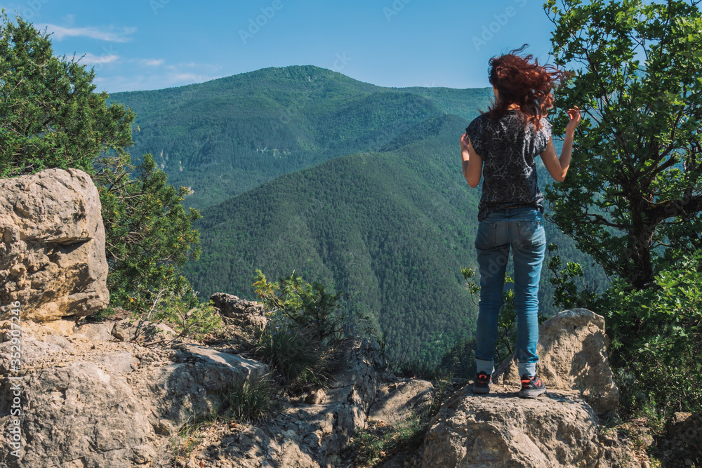 A full body shot of an unrecognizable young Caucasian female hiker standing on a rock in the French Alps mountains on a sunny summer day