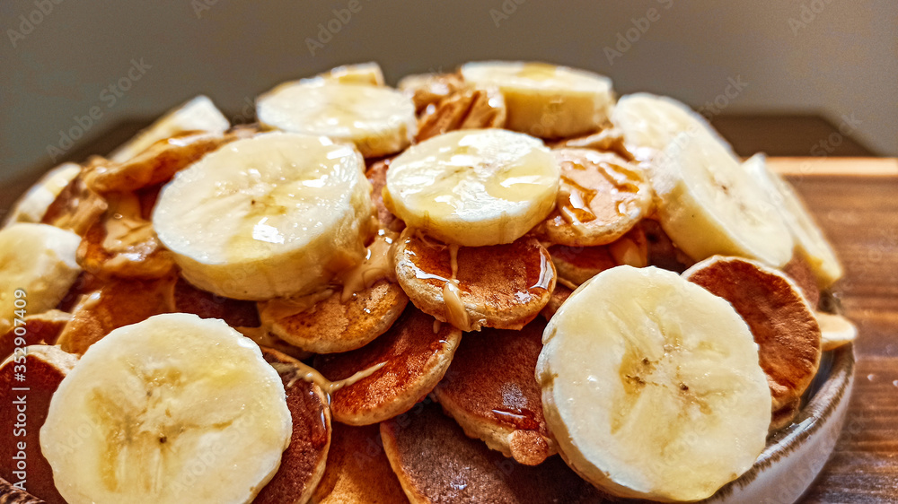 A plate of poffertjes, traditional Dutch Mini Pancakes served with honey, peanut butter and banana on the wooden background
