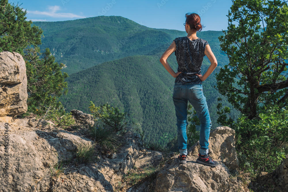 A full body shot of an unrecognizable young Caucasian female hiker standing on a rock in the French Alps mountains on a sunny summer day