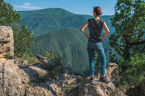 A full body shot of an unrecognizable young Caucasian female hiker standing on a rock in the French Alps mountains on a sunny summer day