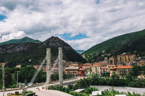 A panoramic wide landscape view of a bridge and an old French town in the valley of Var in the Alps mountains on a cloudy day (Puget-Theniers, Alpes-Maritimes, France)