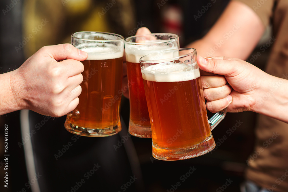 Friends drinking beer at pub. Toast for beer. Men hands raising toast with cold beer mugs at bar. Friends drinking beer at pub. Toast for beer. Men hands raising toast with cold beer mugs at bar.