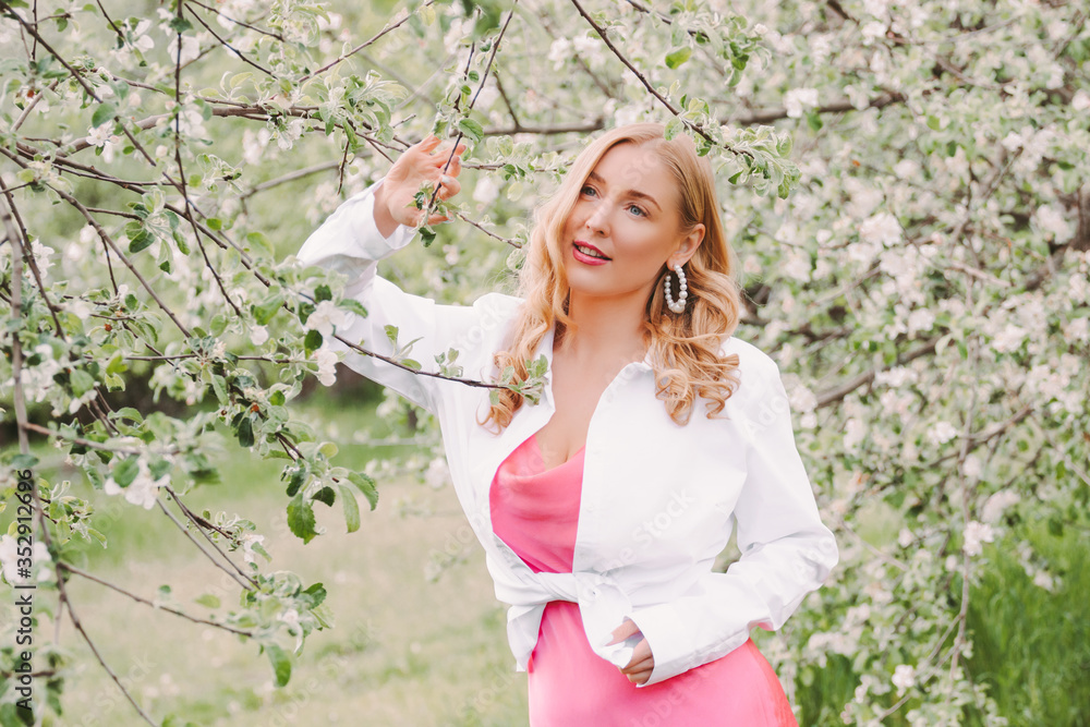 Portrait young beautiful happy woman in white shirt and pink dress relax and smile on green blossom garden. Cheerful attractive stylish blonde hippie girl posing in countryside park. Enjoy nature Portrait young beautiful happy woman in white shirt and pink dress relax and smile on green blossom garden. Cheerful attractive stylish blonde hippie girl posing in countryside park. Enjoy nature