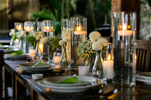 The wooden table is decorated with simple ornaments, dominant clear glass and white flowers for dinner.