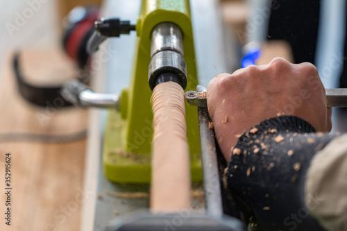 Carpenter man is carving the wooden stick. Spinning wood wheel machine. Trimming forming a round detail. Joiner is using metal tool to make the handmade decoration at workshop.