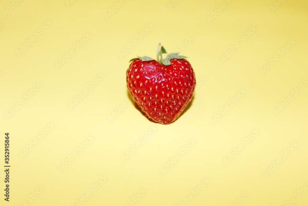 One strawberry in the center isolated on a yellow background with copy space. Fresh strawberry berry top view on a yellow background.