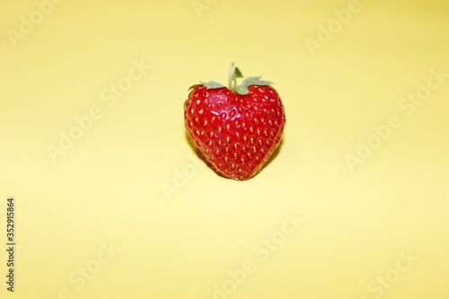 Obraz na płótnie One strawberry in the center isolated on a yellow background with copy space. Fresh strawberry berry top view on a yellow background. w salonie
