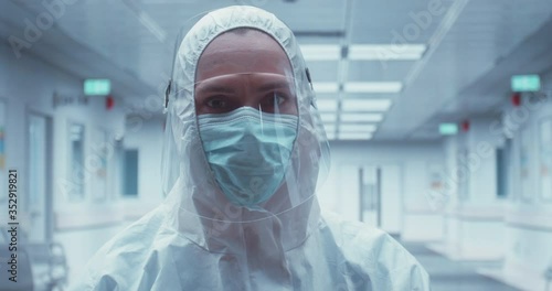 Portrait of Caucasian female doctor posing in a protective suit and face shield in an empty hospitall hallway photo