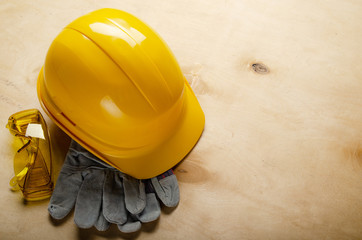 Yellow plastic hard hat glasses and protective gloves laying on plywood. Safe labor concept