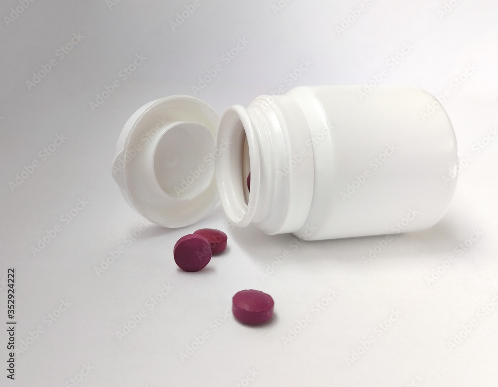 White bottle with purple pills on white background. White bottle with purple pills on white background.