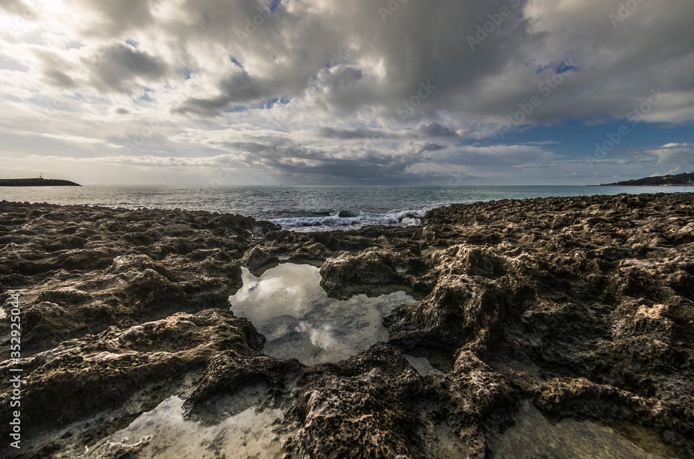 Fototapeta premium Sunset over the sea with rocks and cloudy sky