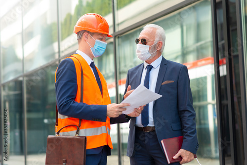 Engineer man with mask discussing something with senior business man with mask