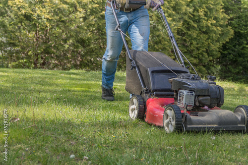 Old red push lawn mower cutting grass in blue jeans sunny shady spring day