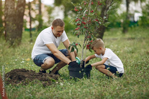 Family on a yard. Father with son planting a tree. Boy with a green funnel © prostooleh