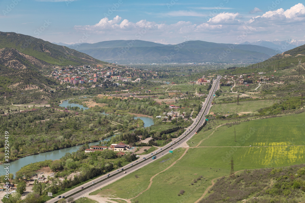 Aerial view on Georgian Military Road and Aragvi river near town of Mtskheta, ancient capital of Georgia. Blue sky with Caucasus mountains on background.