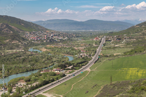 Aerial view on Georgian Military Road and Aragvi river near town of Mtskheta, ancient capital of Georgia. Blue sky with Caucasus mountains on background.