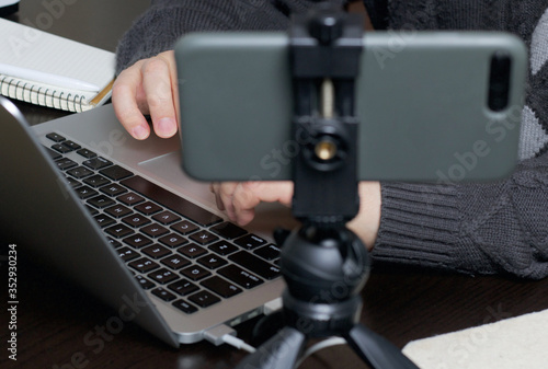 A man works at a laptop. Near the smartphone on a tripod. Hands are taken close up.