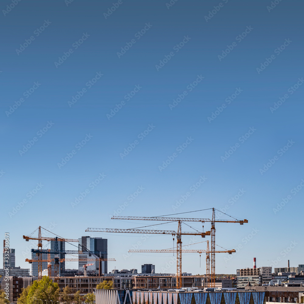 A modern real estate development metropol cityscape with skyscrapers being built by several cranes in the bottm and a lot of copy space on a clear gradient blue sky in the upper part