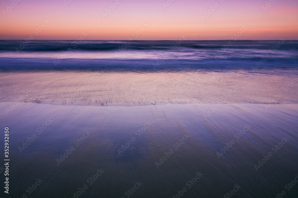 Amazing view of the Atlantic ocean coast at dusk. Long exposure wave and lights reflecting on a sandy beach. Selective focus. Concept minimal landscape.