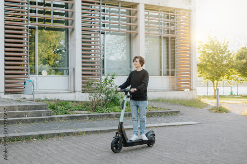 Junger moderner Student fährt entlang der Starße einen E-Scooter bei Sonnenuntergang. Mensch pendelt im Sommer mit Hilfe neuster Technologie der Zukunft. 