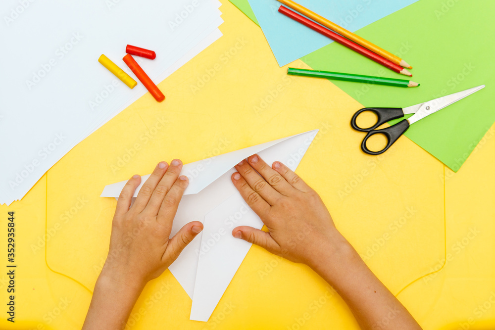 young child boy hands does white paper fly plane on yellow table step to step young child boy hands does white paper fly plane on yellow table step to step