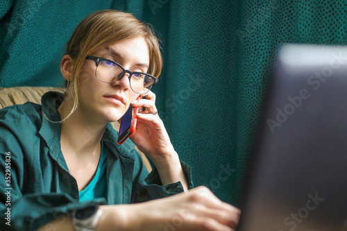 young woman with a phone and laptop works remotely