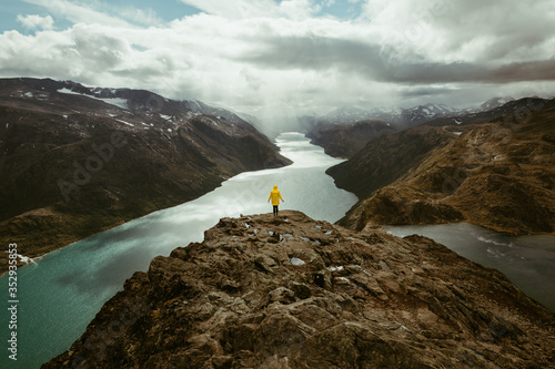 Girl wearing yellow rain coat taking in the view over Norway lake after long hike