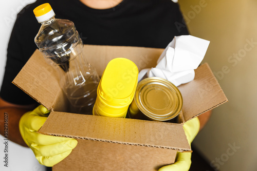 man in yellow rubber gloves keep brown cardboard box with plastic paper and metall rubbish on black t-shirt