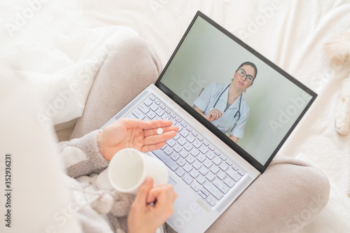 Unrecognizable woman drinks pills and watches a medical video blog on a laptop. A female doctor conducts a distance consultation with a sick patient. Girl with the flu on sick leave.