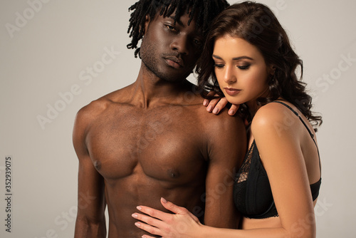 beautiful seductive interracial couple hugging isolated on grey