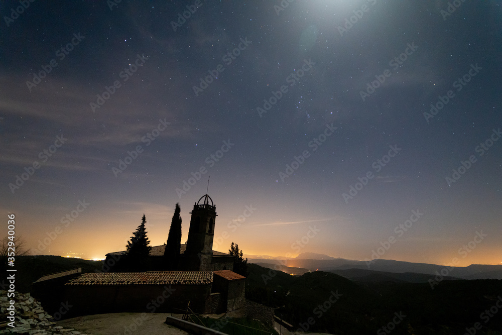 Naklejka premium Stars shining begin the church of Sant Miquel de Castelltallat. In the background of the images the mountain of Montserrat. The most famous mountain in Catalonia.