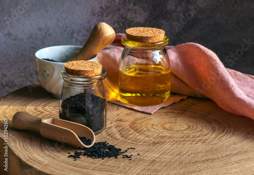 Black cumin seeds and a wooden spoon, bottle of black seed oil on a wooden table. Healthy, vegetarian, organic food concept.