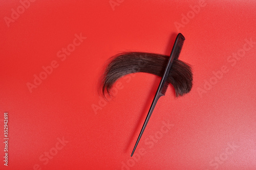 a cut-off lock of brown hair lies in a comb comb on a red background. shiny hair with split ends stuck in the comb