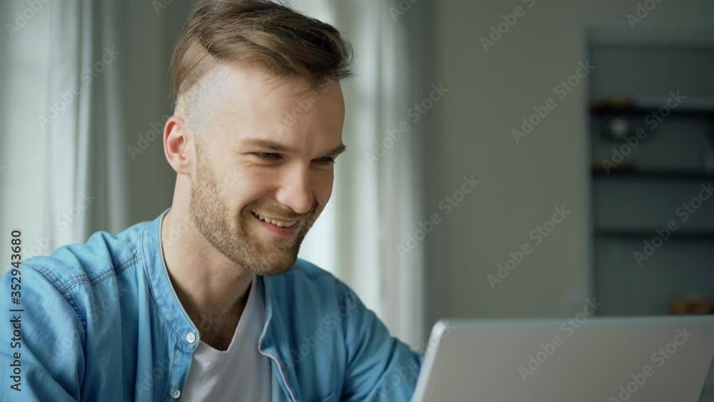Medium side view shot of handsome young man opening laptop computer, smiling and day dreaming at home Medium side view shot of handsome young man opening laptop computer, smiling and day dreaming at home
