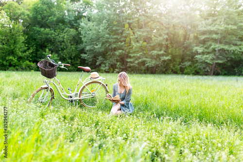 Girl is reading a book on a background of an old bicycle. Active leisure in the park. photo
