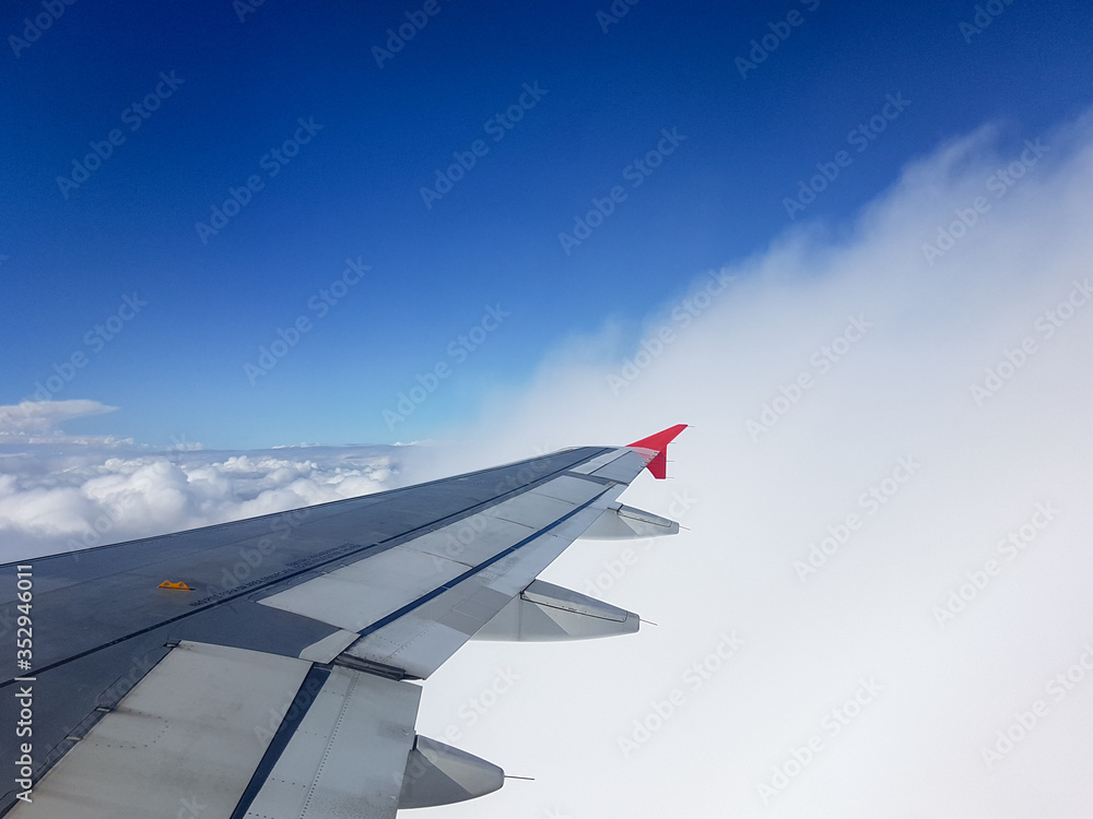 Fototapeta premium From the window of the plane in mid-flight you can see its wing between clouds in an intense blue sky.