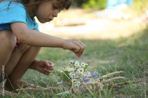 Little girl creating composition of sand, flowers and plants